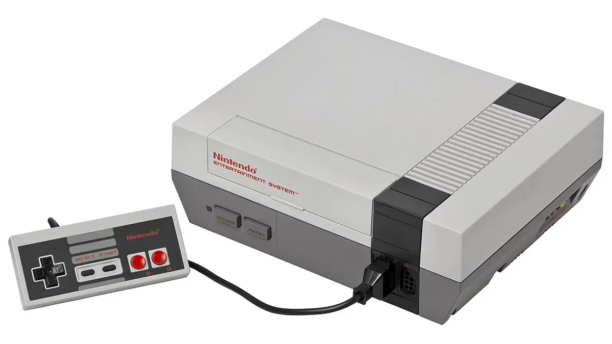 Console Nintendo NES grigia con controller rettangolare collegato.