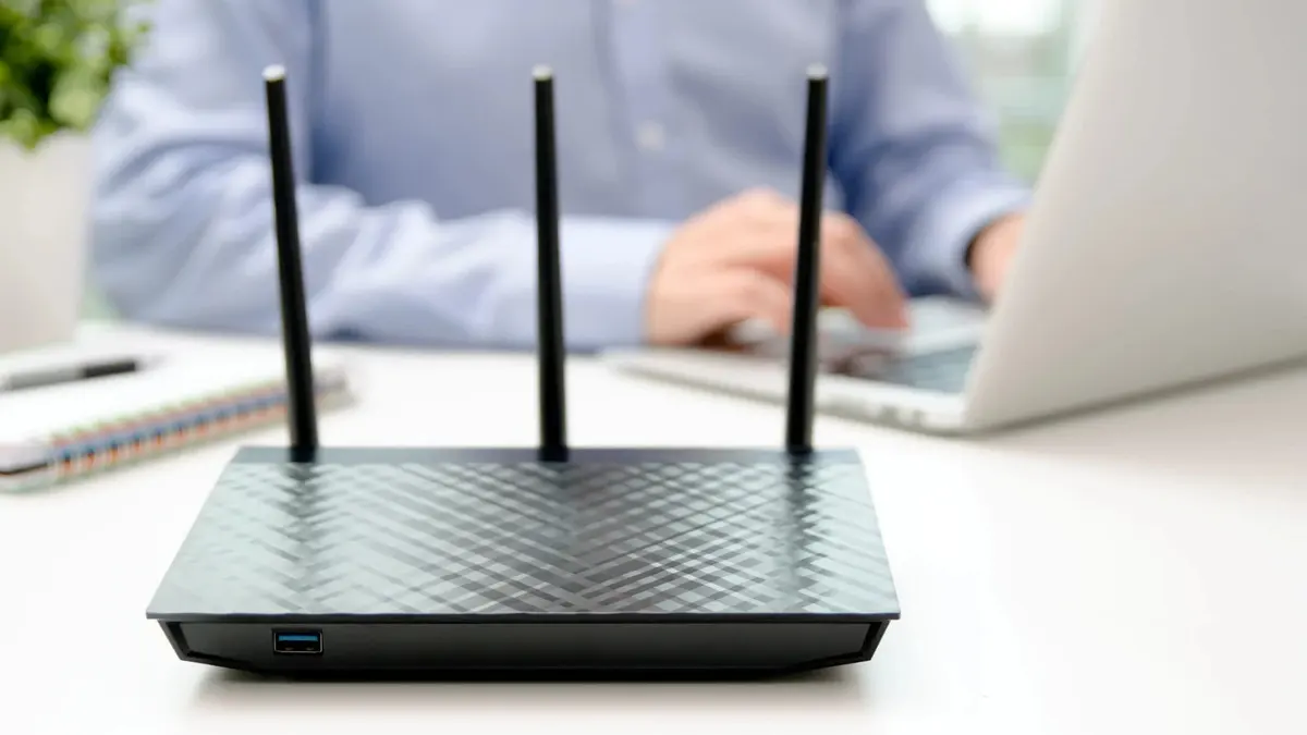 Router wireless con tre antenne davanti a una persona che usa un portatile.